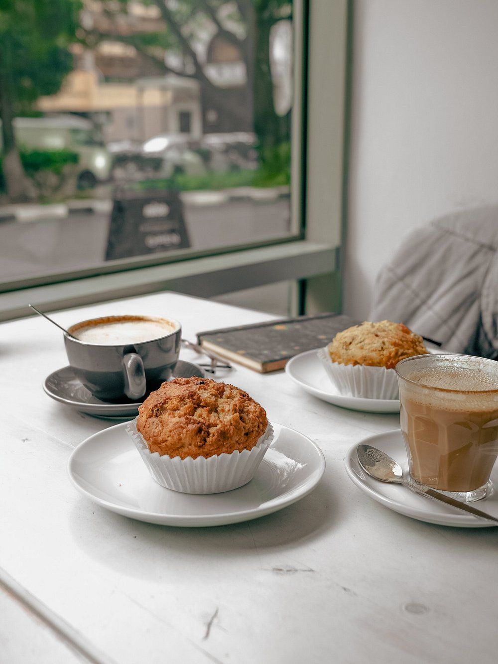 A table with a cup of coffee, a muffin, and a glass of coffee.