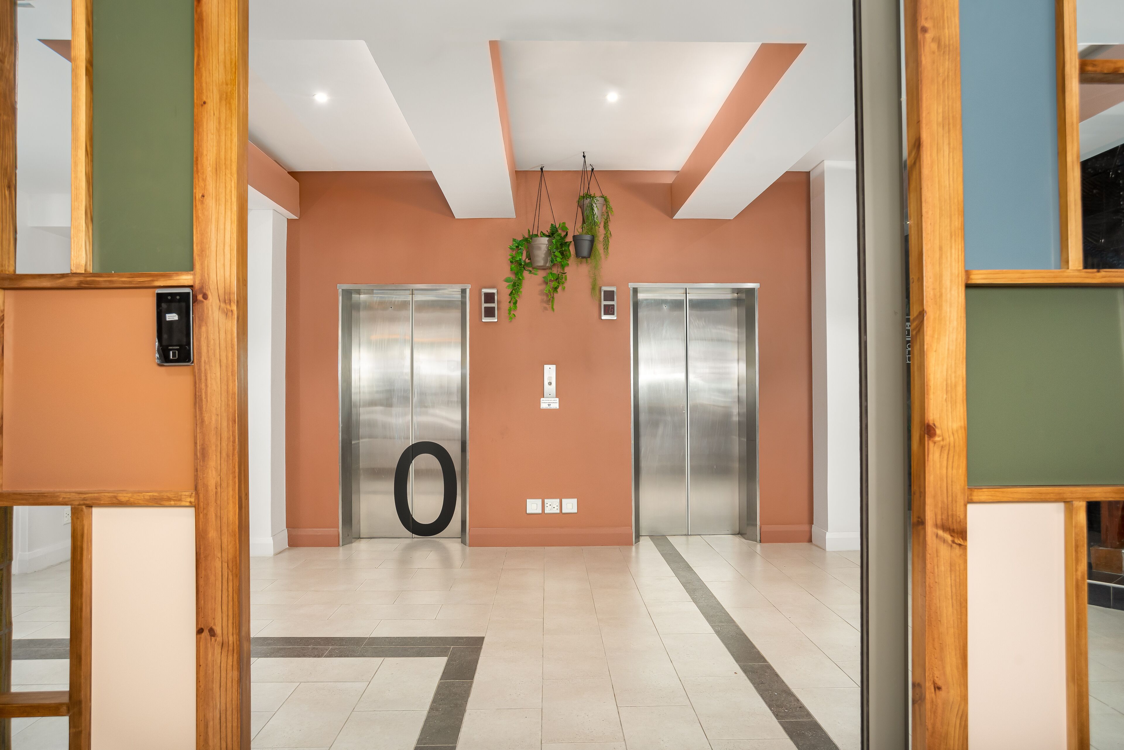 A modern elevator area with two elevators, a visible handrail, and a wall-mounted planter with greenery.