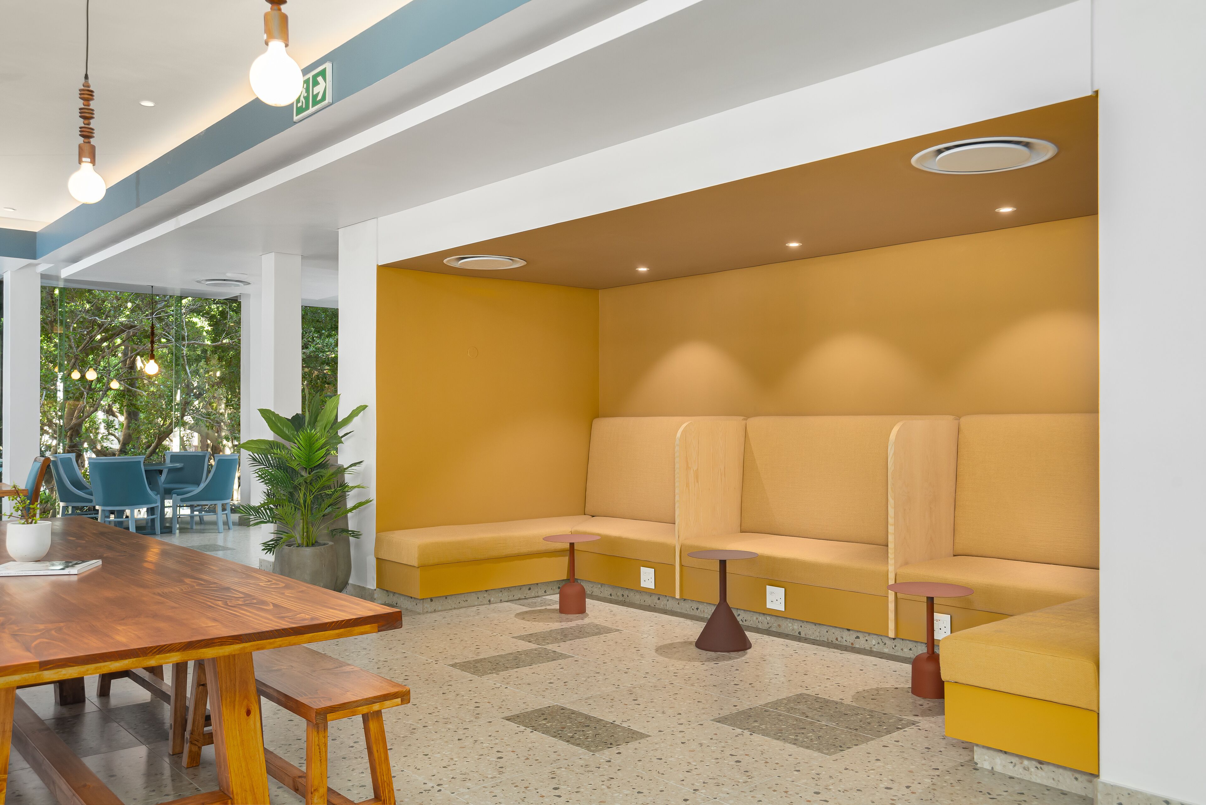 A modern waiting area with a wooden table, benches, and a yellow sofa.