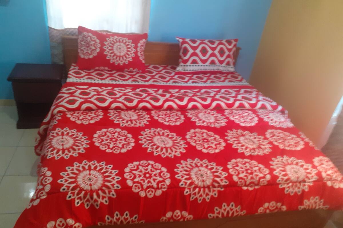 A bed with a red and white patterned bedspread, a wooden headboard, and a nightstand with a lamp.