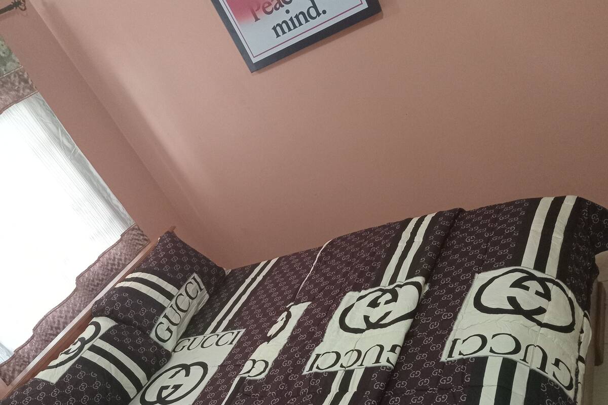 A bed with a patterned blanket and pillows, a framed picture on the wall, and a window with curtains.