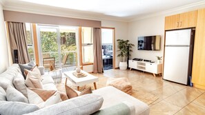 A modern living room with a sofa, coffee table, and TV. There is a balcony with a view of greenery. - MONTEREY - relaxed living for couples in Bright (Bright)