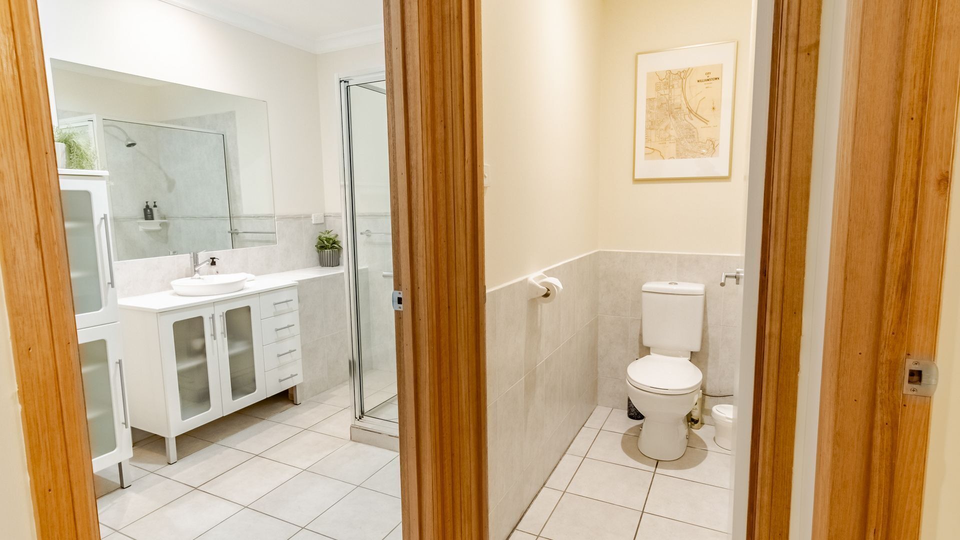A modern bathroom with a glass shower enclosure, a white sink with a mirror above, and a toilet with a map on the wall.