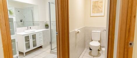 A modern bathroom with a glass shower enclosure, a white sink with a mirror above, and a toilet with a map on the wall.