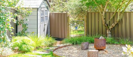 A garden with a shed, wooden fence, and a fire pit.