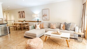 Un salon moderne comprenant un canapé, un pouf, une table basse et un coin repas avec des chaises et une table.