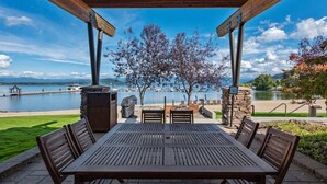 A covered outdoor dining area with a view of a lake and boats. - Seasons Lakefront Escape | Pool, Hot Tub & Views (Sandpoint)
