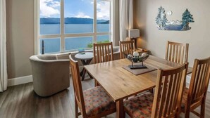 A dining area with a wooden table and chairs, a view of a lake, and a decorative wall piece. - Seasons Lakefront Escape | Pool, Hot Tub & Views (Sandpoint)