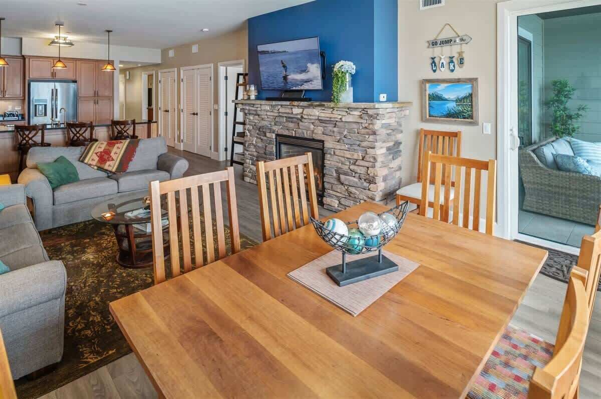 A cozy living room with a fireplace, a dining table with chairs, a sofa, and a television mounted on the wall.