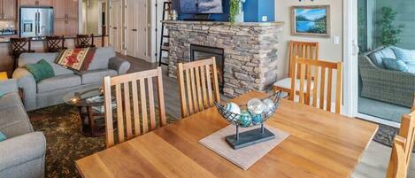 A cozy living room with a fireplace, a dining table with chairs, a sofa, and a television mounted on the wall.