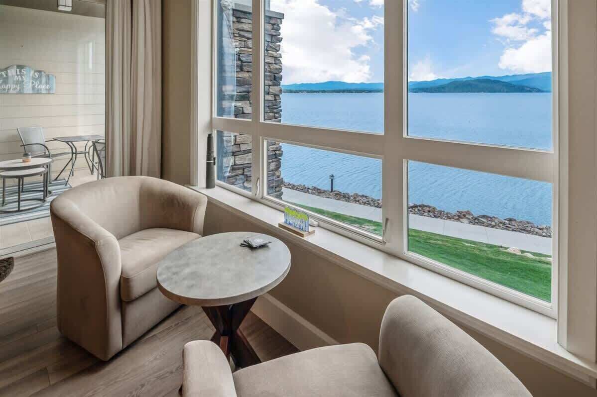 Habitación con un ventanal grande que ofrece vistas a un lago y montañas. Hay dos sillas y una mesita.