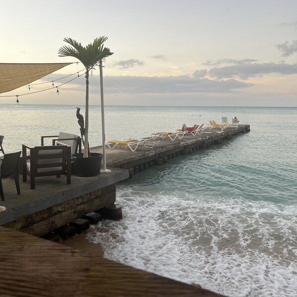 A pier with lounge chairs and a table, overlooking the sea.