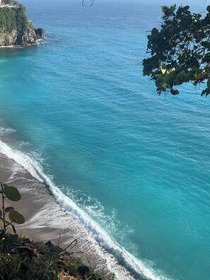 A coastal beach with clear turquoise waters and a rocky cliff.