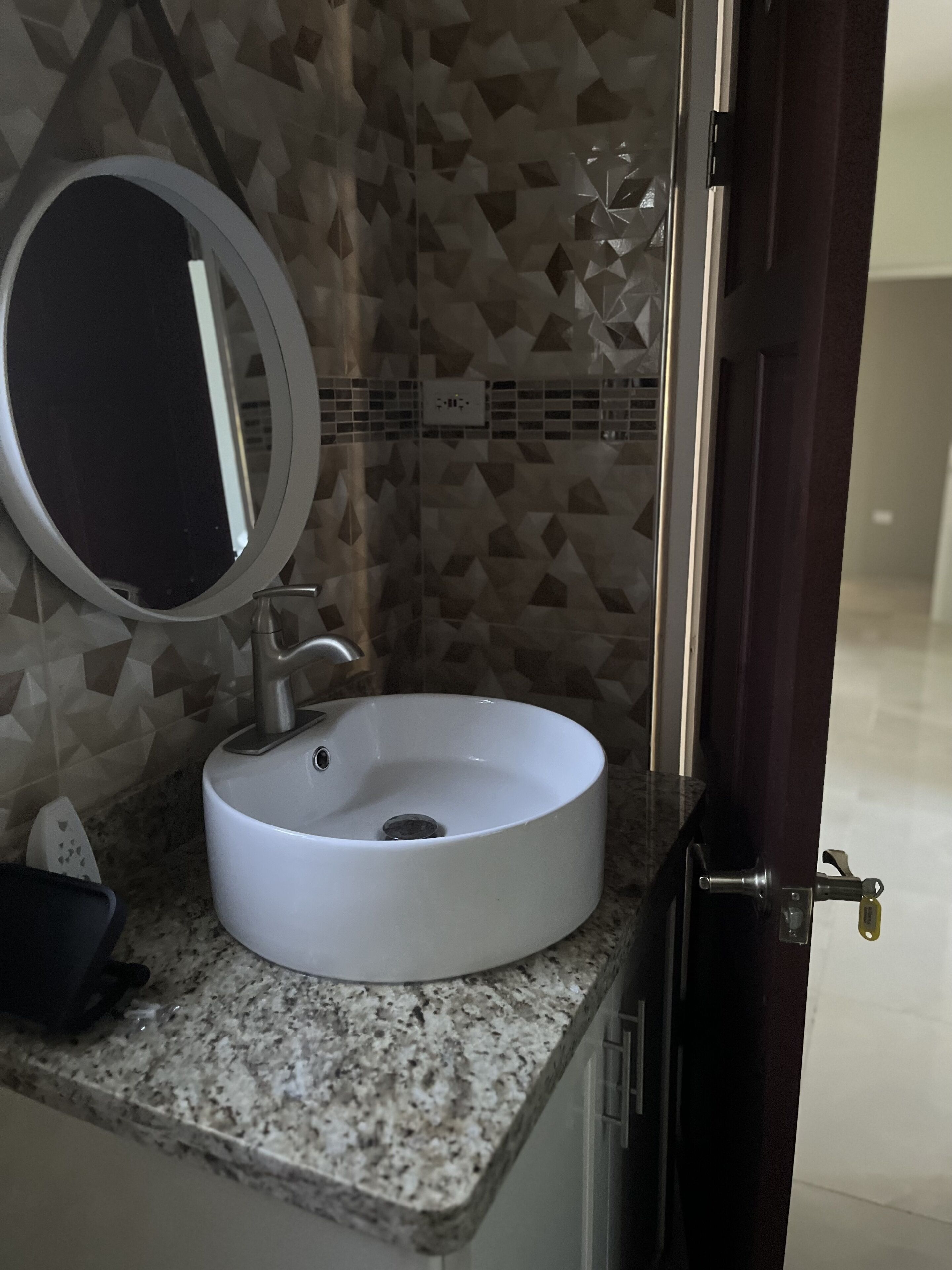 A bathroom with a white sink, a round mirror, and a geometric tile backsplash.
