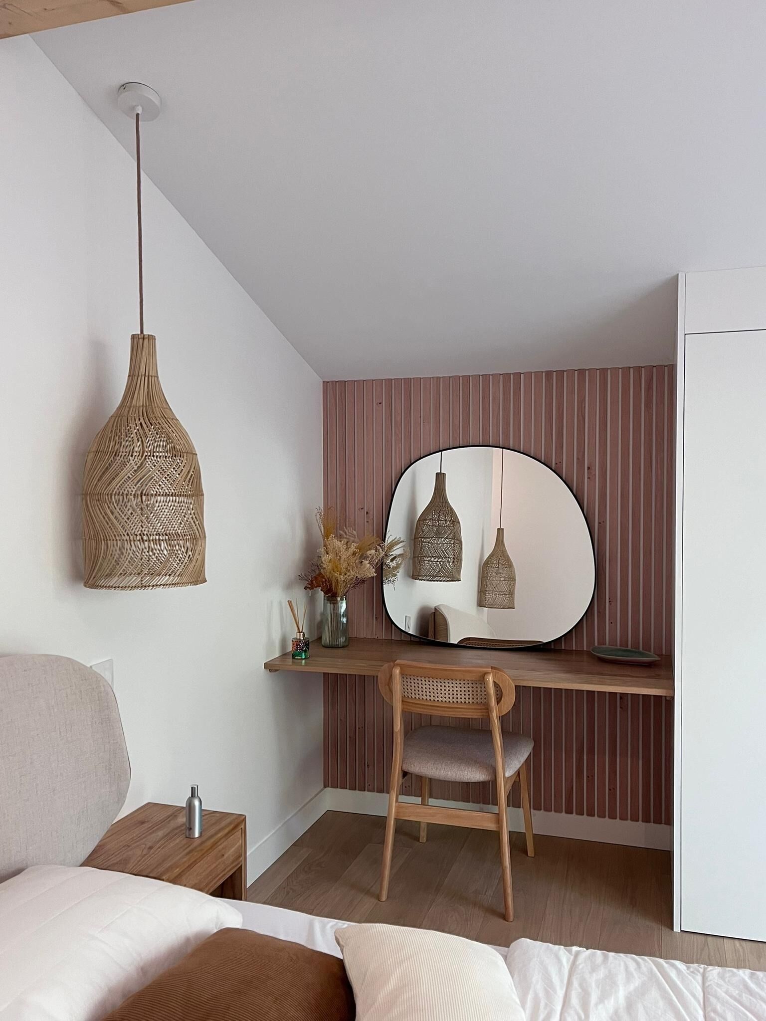A bedroom with a bed, a desk with a chair, a mirror, and a hanging light fixture.