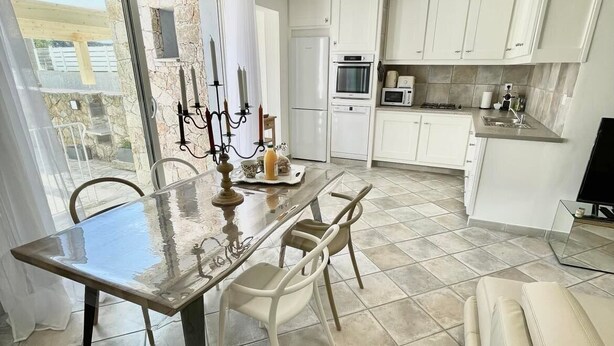 Una cocina moderna con armarios blancos, un comedor con mesa de vidrio y un sofá.