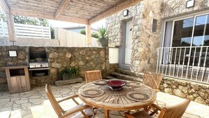 Un patio exterior con una mesa redonda de madera, cuatro sillas y un muro de piedra de fondo.