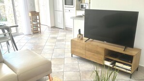 Una sala moderna con televisor de pantalla plana, una mesa de centro de madera con objetos decorativos, un sofá de cuero y un comedor con mesa y sillas.