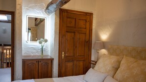 Une chambre avec une porte en bois, un miroir, une table de chevet avec une lampe et un lit avec des oreillers.