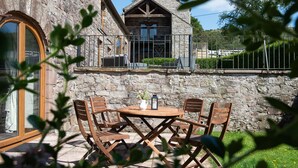 Un bâtiment en pierre doté d’un balcon, une table en bois avec des chaises et une fenêtre avec des rideaux.