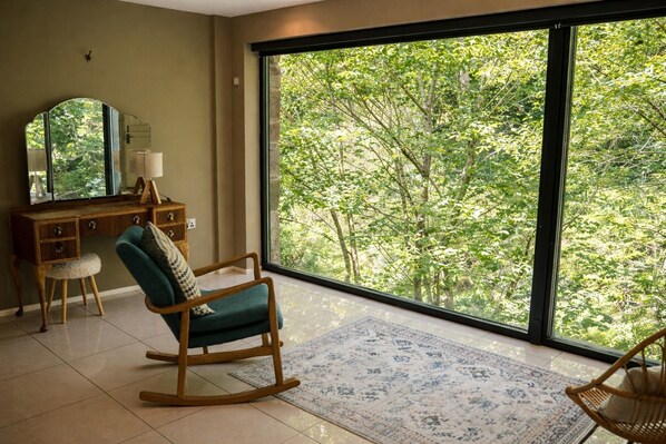 A room with a large window, a rocking chair, a desk with a mirror, and a patterned rug.