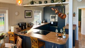A modern kitchen with a wooden island, dark blue cabinets, and copper pots hanging from the ceiling. - Green Vale Lodge, Yanwath, dog friendly with hot tub, close to Lake Ullswater (Yanwath)