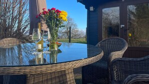 A round glass table with wicker chairs, a vase of flowers, and wine glasses. - Green Vale Lodge, Yanwath, dog friendly with hot tub, close to Lake Ullswater (Yanwath)