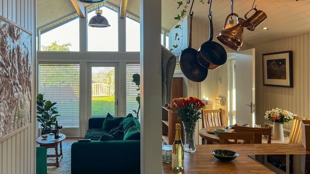 A cozy living room with a green sofa, a dining area with a wooden table, and a kitchen with hanging copper pots. - Green Vale Lodge, Yanwath, dog friendly with hot tub, close to Lake Ullswater (Yanwath)