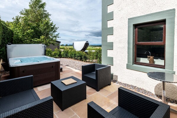 An outdoor patio with a hot tub, wicker furniture, and a window with a view of the countryside.