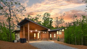 Ein modernes Blockhaus mit einer großen Veranda, umgeben von Bäumen und einer Schotterzufahrt.
