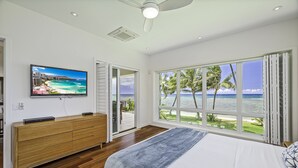 A bedroom with a large bed, a TV on a wooden dresser, and a view of the ocean through large windows. - Hula House - Beachfront North Shore - NEW SPECIAL FALL RATES. (Wailua)