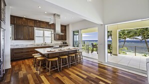 A modern kitchen with a large island and bar stools, a view of the ocean, and a spacious balcony. - Hula House - Beachfront North Shore - NEW SPECIAL FALL RATES. (Wailua)