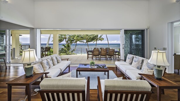 A spacious living room with a large window overlooking the ocean, furnished with a sofa, chairs, and a coffee table. - Hula House - Beachfront North Shore - NEW SPECIAL FALL RATES. (Wailua)