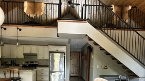 A spacious kitchen with a central island, a dining area with a wooden table and chairs, and a staircase leading to an upper level. - Upper Hamlin Lake Cabin (Free Soil)