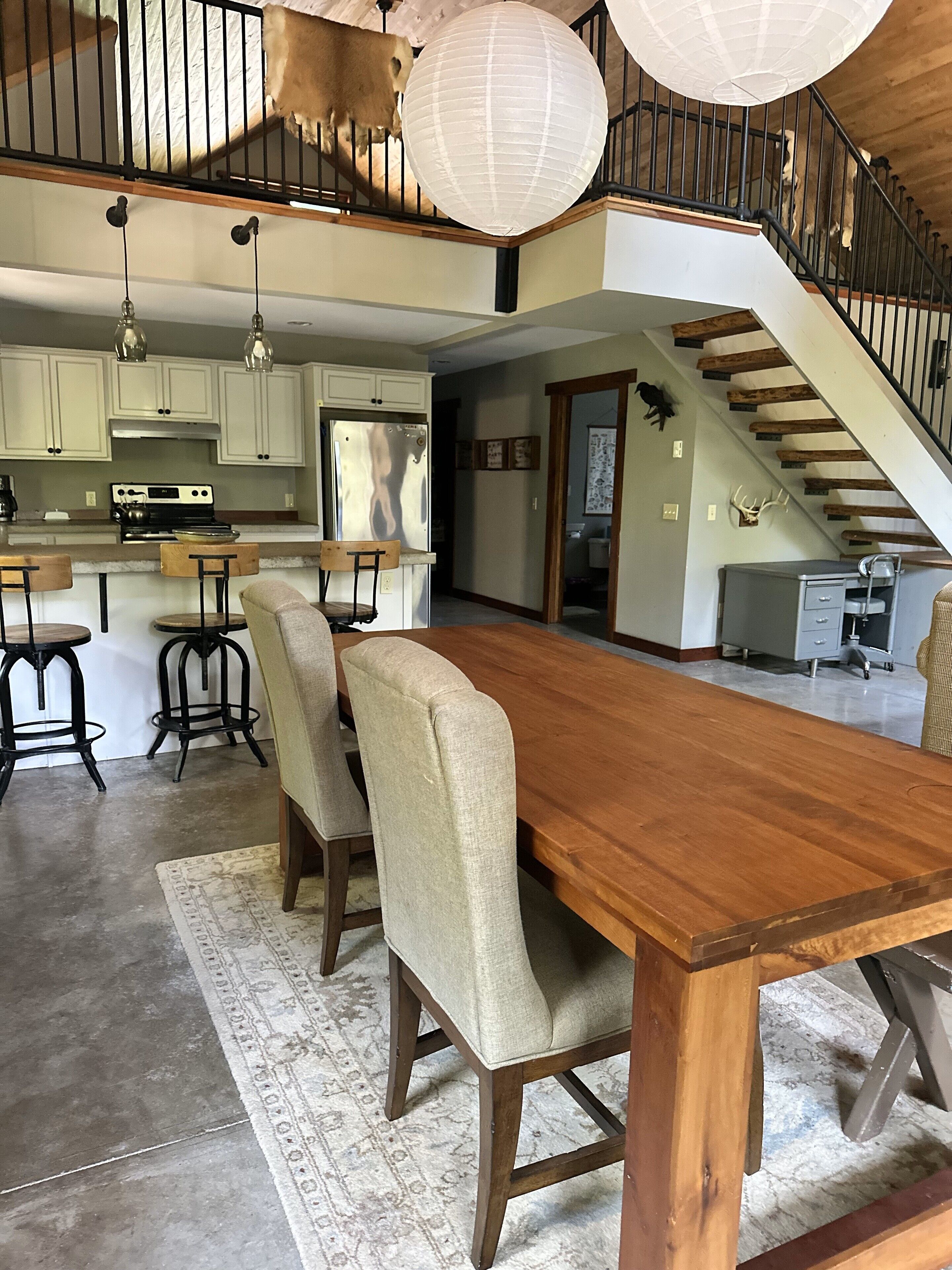 A spacious kitchen with modern appliances, a dining area with a large wooden table and four chairs, and a staircase leading to an upper level.
