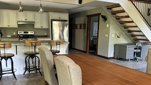 A spacious kitchen with modern appliances, a dining area with a large wooden table and four chairs, and a staircase leading to an upper level. - Upper Hamlin Lake Cabin (Free Soil)