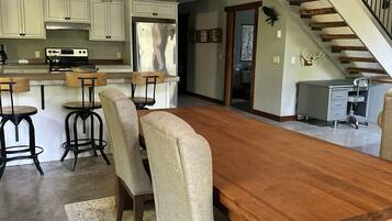 A spacious kitchen with modern appliances, a dining area with a large wooden table and four chairs, and a staircase leading to an upper level.