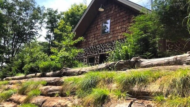 A rustic building with a sloped roof, surrounded by lush greenery and a rocky foreground. - Upper Hamlin Lake Cabin (Free Soil)