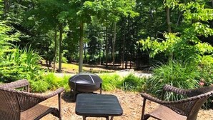 An outdoor seating area with wicker chairs and a table, surrounded by dense greenery and trees. - Upper Hamlin Lake Cabin (Free Soil)