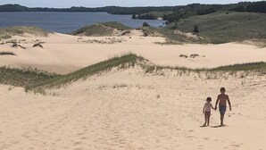 A sandy beach with dunes and a body of water in the background. - Upper Hamlin Lake Cabin (Free Soil)