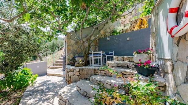 Una escalera de piedra lleva a una zona de estar con un muro de piedra y plantas en macetas.