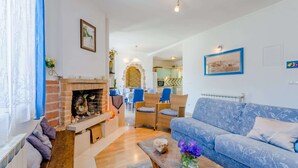 Una sala de estar con chimenea, un sofá azul y un comedor con sillas de mimbre.