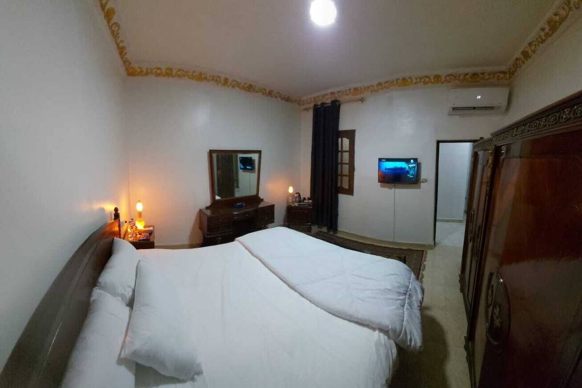 A hotel room with a bed, bedside tables, a mirror, a TV, and a wardrobe.