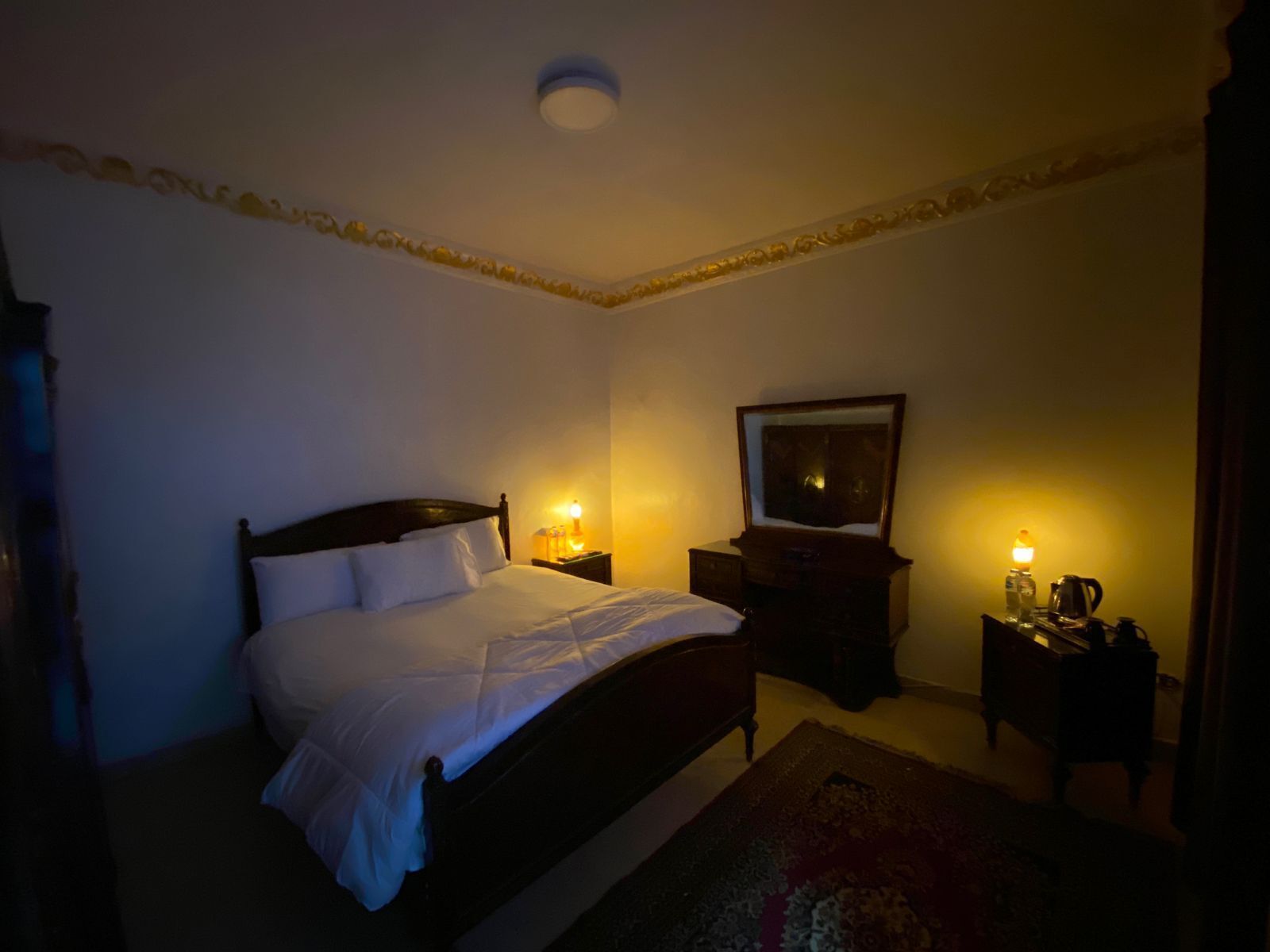 A dimly lit hotel room with a single bed, a nightstand, a dresser, and a mirror.