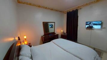 A hotel room with a bed, a dresser, a mirror, a television, and a nightstand with a lamp.