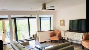 Een moderne woonkamer met een grote hoekbank, een fauteuil, een glazen salontafel en een televisie op een kast.