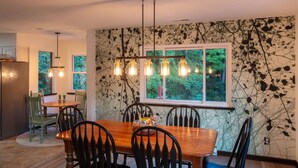 Een eetgedeelte met een houten tafel en stoelen, een hanglamp en een raam met uitzicht op groen.