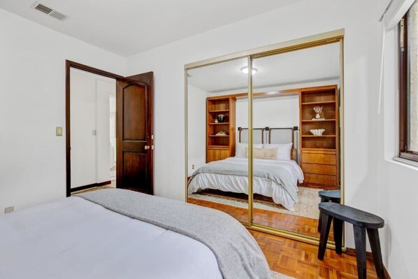 A bedroom with a large mirror, wooden wardrobe, and a bed.