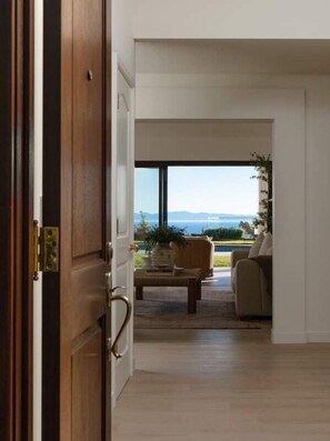 A room with a wooden door, a view of a pool and outdoor furniture, and a clear sky.