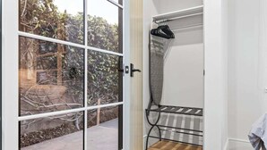 Een kamer met een schuifdeur van glas naar een buitenruimte, een metalen droogrek en een witte muur.